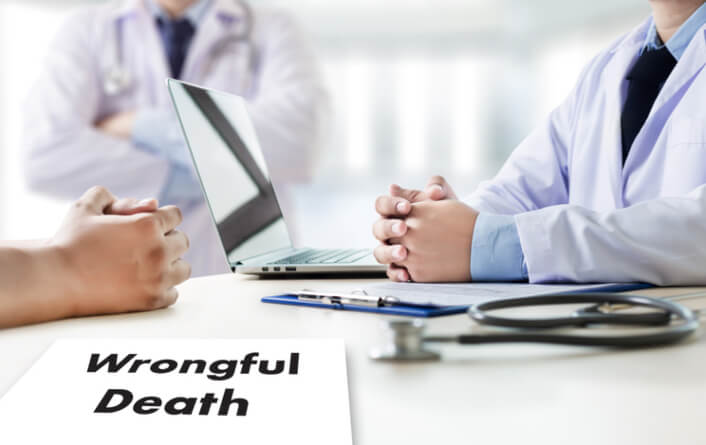 Two medical doctors at a table with laptop stethoscope and form with words wrongful death written