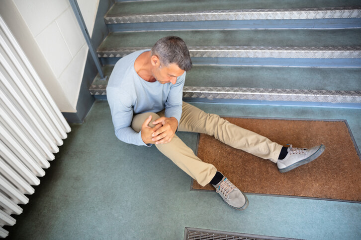 man holding knee sitting on ground in front of staircase after slip and fall accident 