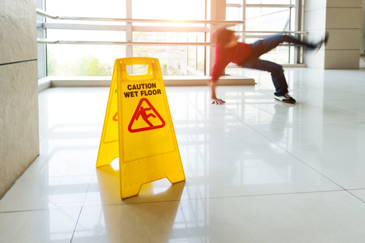 Man slips falling on wet floor next to wet cautious wet floor sign