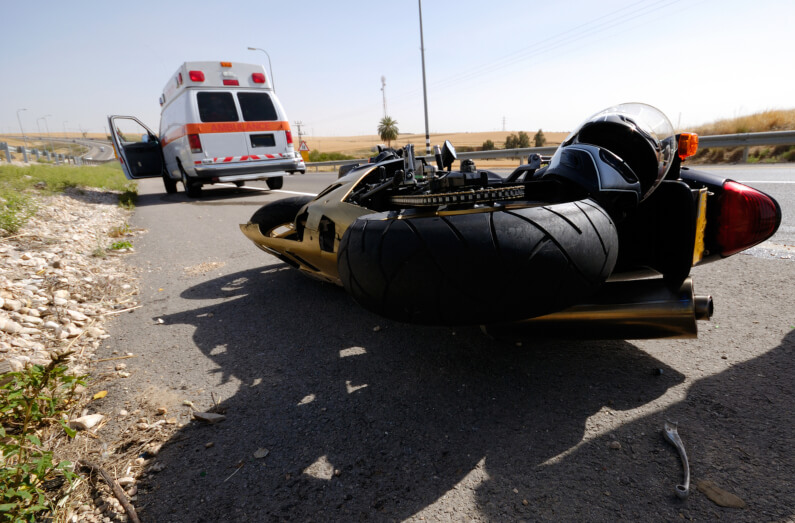 A motorcycle laying on road behind ambulance after a motorcycle accident