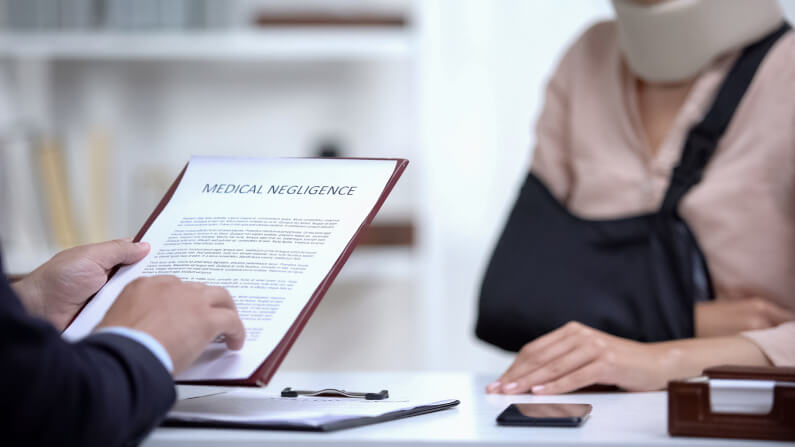 Man sitting across from an injured woman holding clipboard paper saying Medical negligence