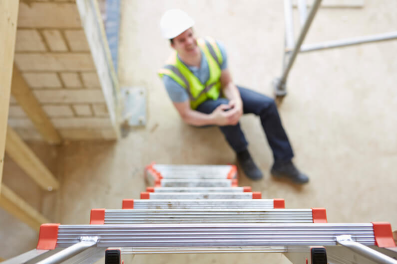 Construction worker sitting on ground holding knee after falling off a ladder on work site