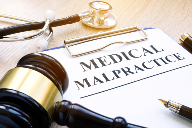 A gavel and stethoscope laying on top of clipboard with paper saying medical malpractice 