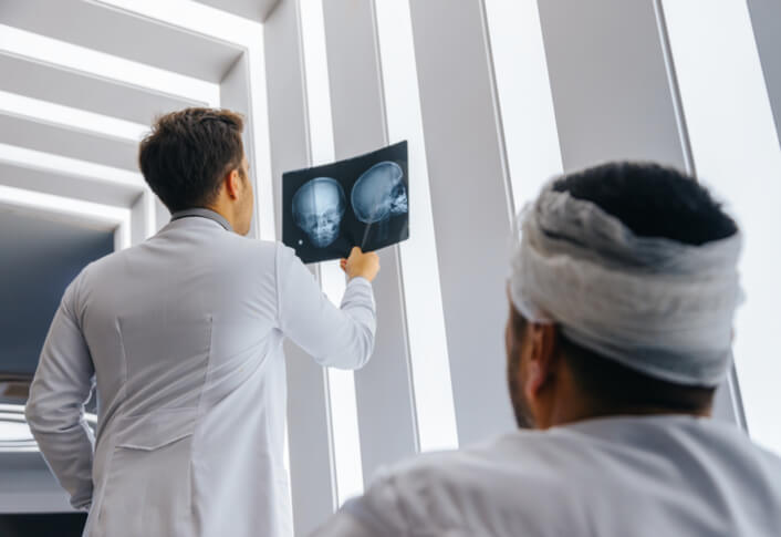 Man with bandaged head waits as doctor reviews scan results for brain injury