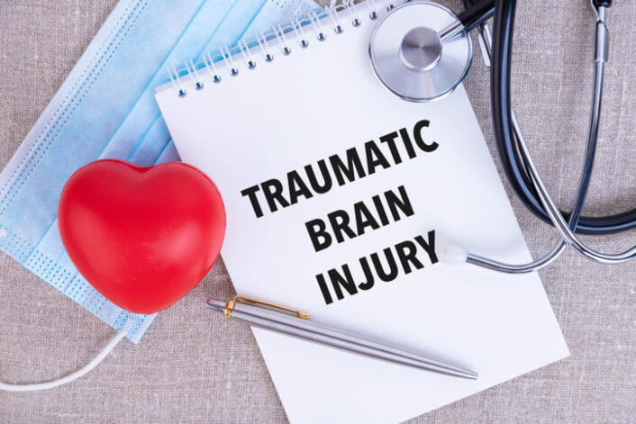 Traumatic brain injury text is written on a notebook, next to a pen, a disposable medical mask and a stethoscope